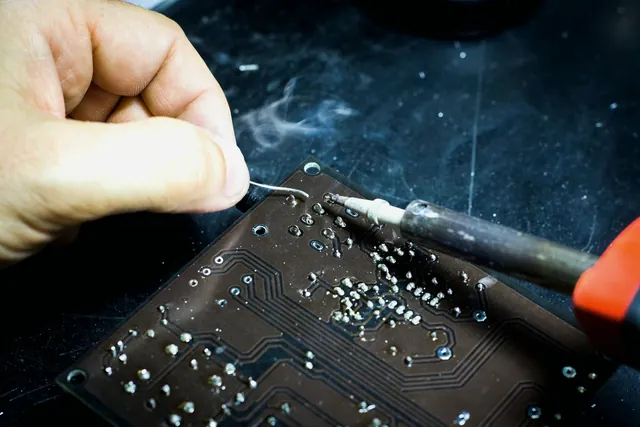 Hands applying a soldering iron to a printed circuit board