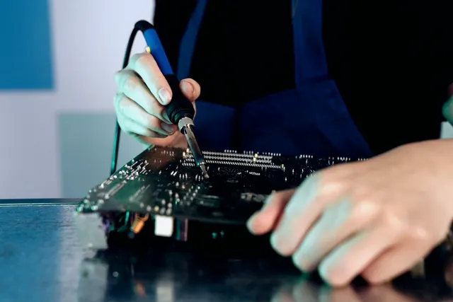 Hands soldering electronic components on a PCB at a workbench