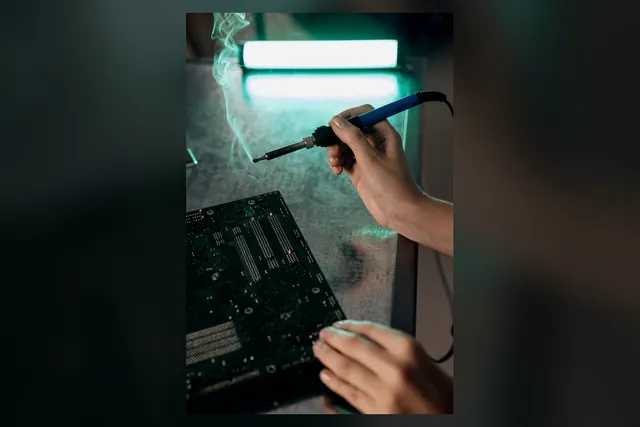 Hands soldering a PCB with visible flux smoke extraction lighting
